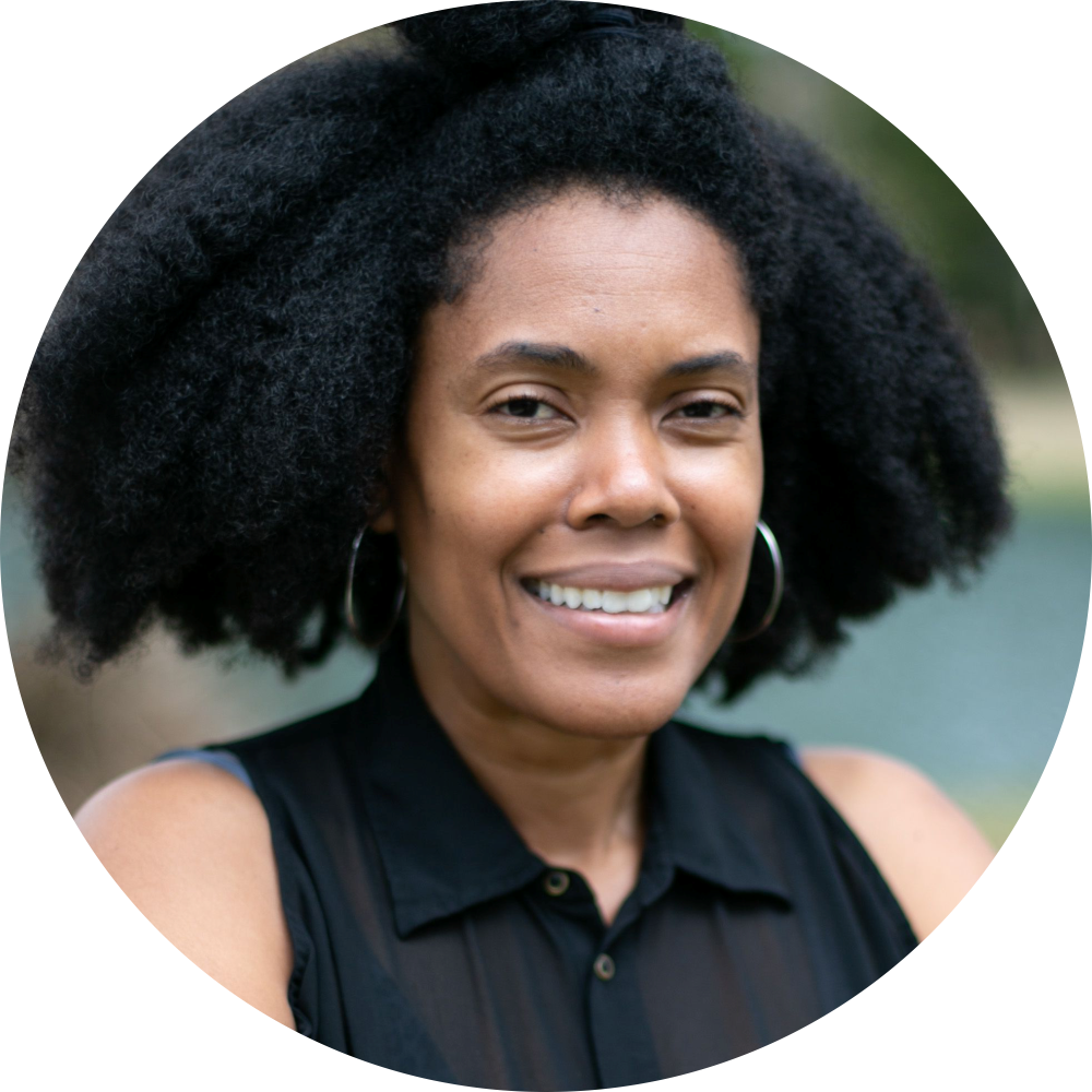 A woman with an afro and hoop earrings smiles for the camera