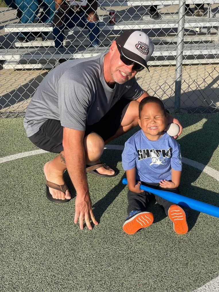 A man is kneeling down next to a little boy holding a baseball bat.