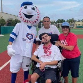A man in a wheelchair is standing next to a mascot on a baseball field.