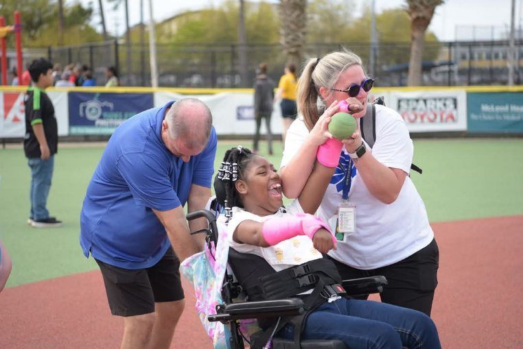 A woman in a wheelchair is being helped by two people.