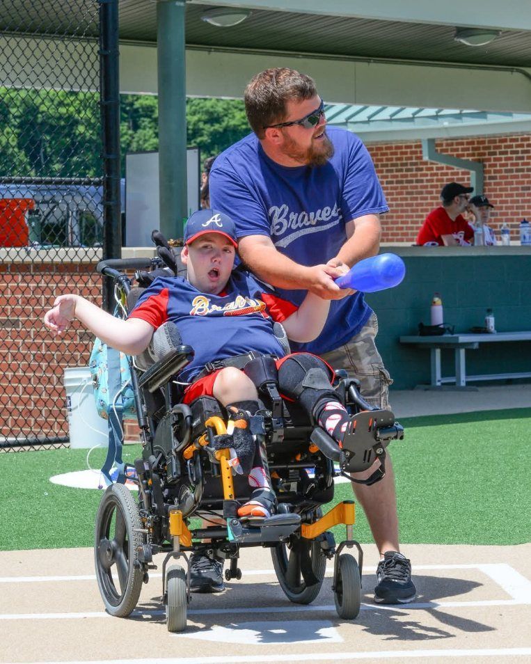 A man in a brewers shirt is standing next to a boy in a wheelchair