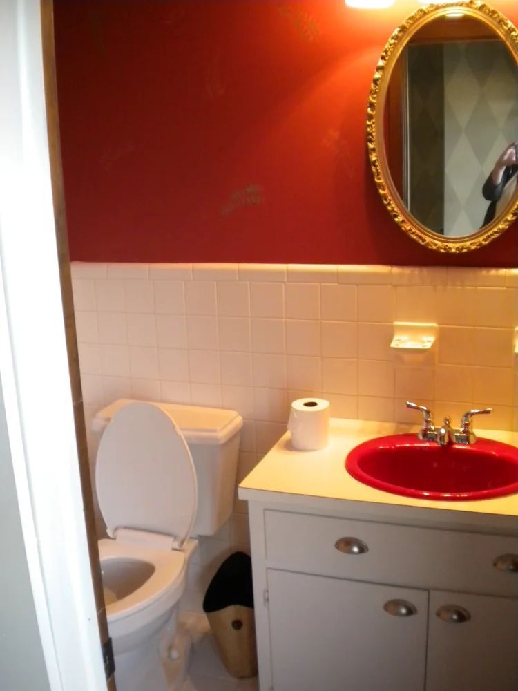 Red and white bathroom with toilet, sink, and mirror.