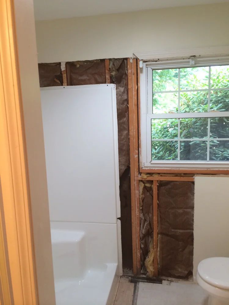 Bathroom under renovation, featuring a partially exposed wall with insulation, bathtub, and window.