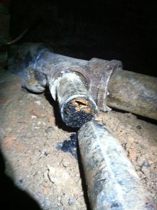 A broken pipe with corrosion and dark residue, resting in dirt.
