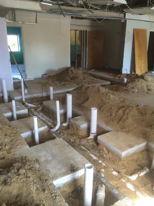 Interior view of a construction site, plumbing pipes exposed in trenches.