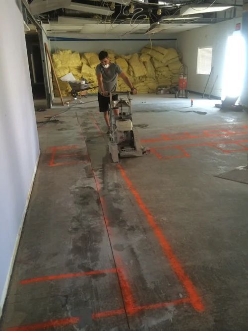 Man operating floor grinding machine in a construction zone, orange lines marking the floor.