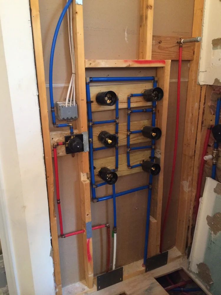 Plumbing system installation in a wall: blue and red pipes connected to black valves. Wooden frame.