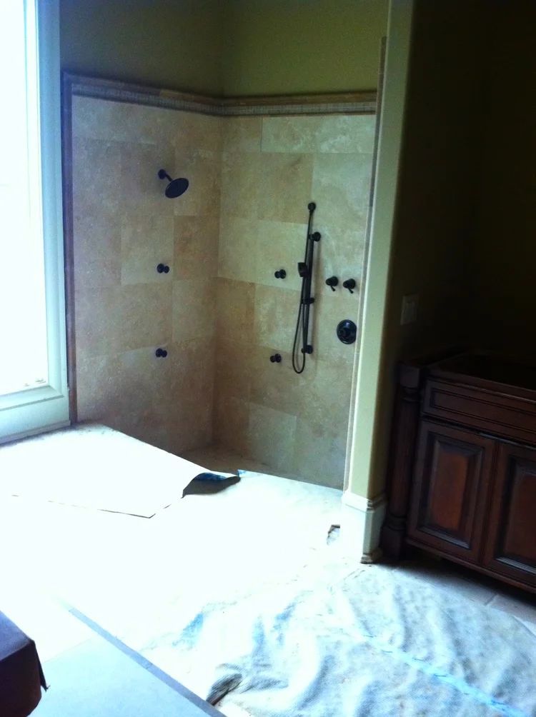 Beige tile shower with dark fixtures; white floor and cabinet.