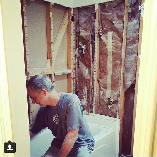 Man working on a bathroom remodel, removing walls around a bathtub.