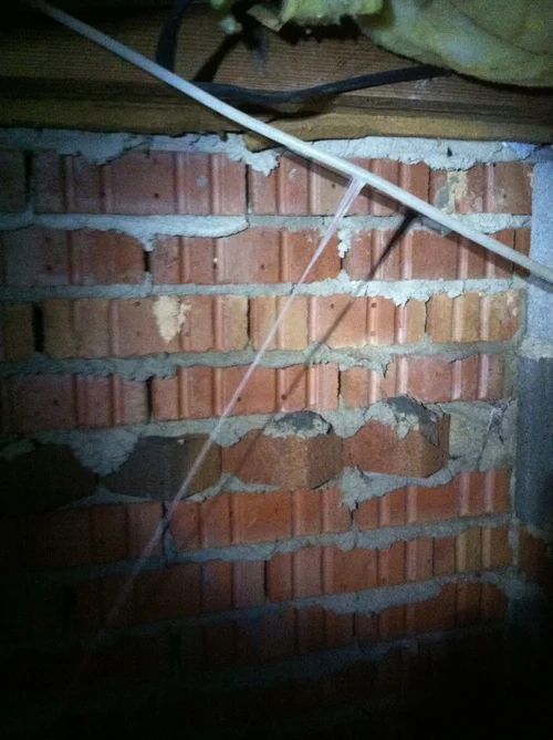Brick wall with mortar, some bricks cracked, viewed from underneath.