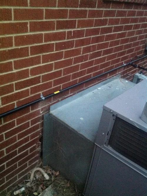 Black conduit along a brick wall, above an air conditioning unit.