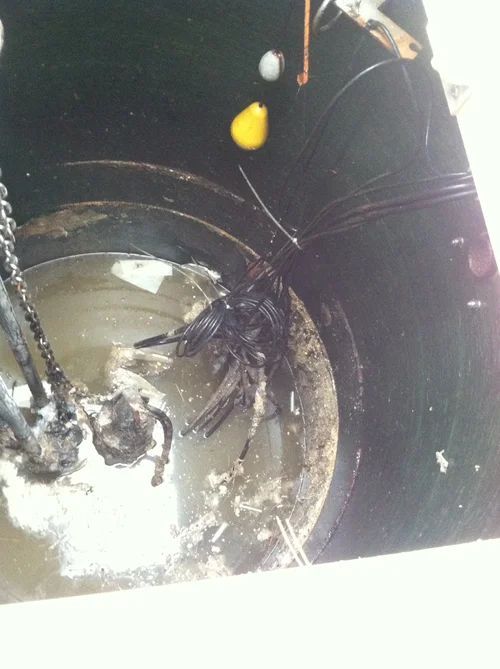 Dark, dirty sump pit with pump and debris floating in the water; cords and chains visible.