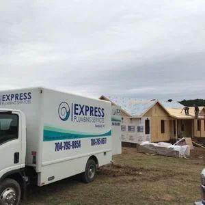 Express Plumbing Services truck at a construction site with workers building homes.