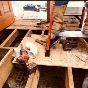 Construction worker standing on plywood, tools scattered on floorboards.