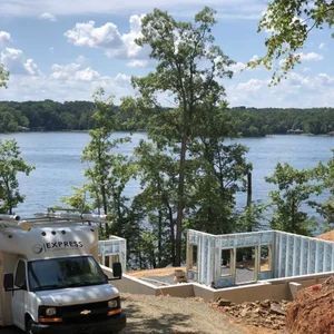 RV parked near a lake house under construction on a sunny day.