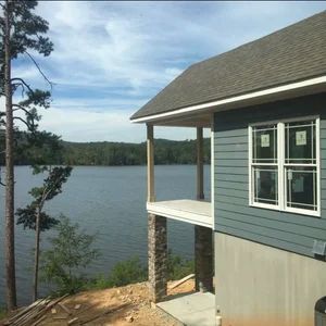 Lake house under construction, blue siding, small porch, view of lake and trees.