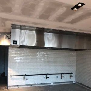 Stainless steel commercial kitchen exhaust hood above white tiled wall, black pipe rack.