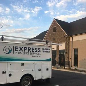 White Express Plumbing Services truck parked in front of a brick building, under a blue sky.