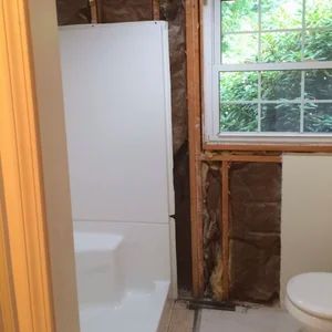Bathroom remodel: white tub and walls, exposed framing, window with a view, toilet.