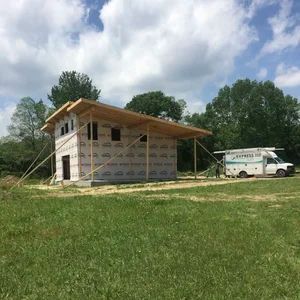 House under construction on a grassy field, supported by temporary beams, with a work van nearby.