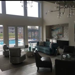 Living room with pool view: blue sofa, gray chairs, glass coffee table, and large windows.