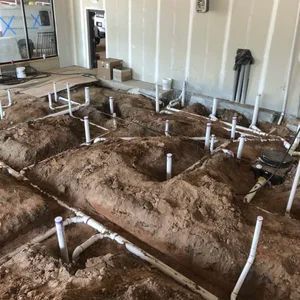 Under-construction plumbing with white pipes and dirt mounds inside a building.