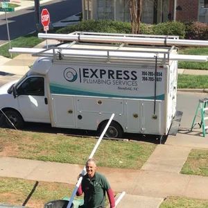 A white Express Plumbing Services truck parked on a street with a man holding PVC pipes.