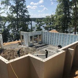Construction site with workers building a concrete foundation near a lake, trees in the background.
