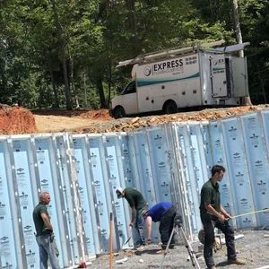 Construction workers near a foundation wall with a utility van labeled 