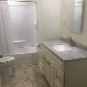 Bathroom with white shower, vanity, toilet, and beige tiled floor.