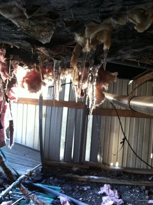 Pink insulation and icicles hanging from under a building, next to a metal wall and wood.