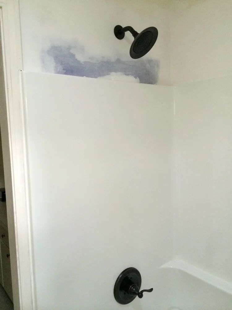 White shower with black fixtures; a patch of blue paint is visible above.