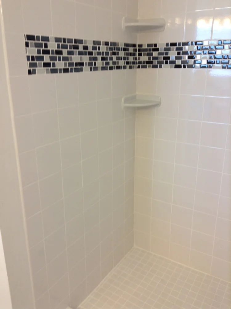 Tiled white shower with a mosaic tile border. Two built-in shelves are visible.