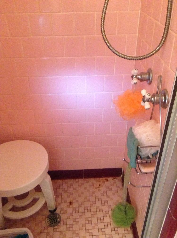 Pink tiled shower with a stool, showerhead, and toiletries.