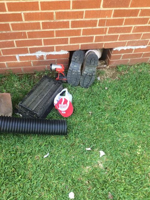 Person inside brick wall opening, feet visible. Tools, debris on grass.
