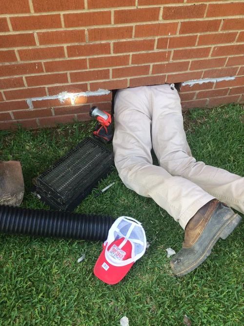 Person's legs sticking out of a brick wall opening. A screwdriver and materials are nearby on the grass.