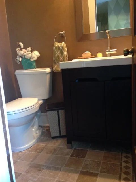 Small bathroom with brown walls, white toilet, black vanity, and patterned floor.