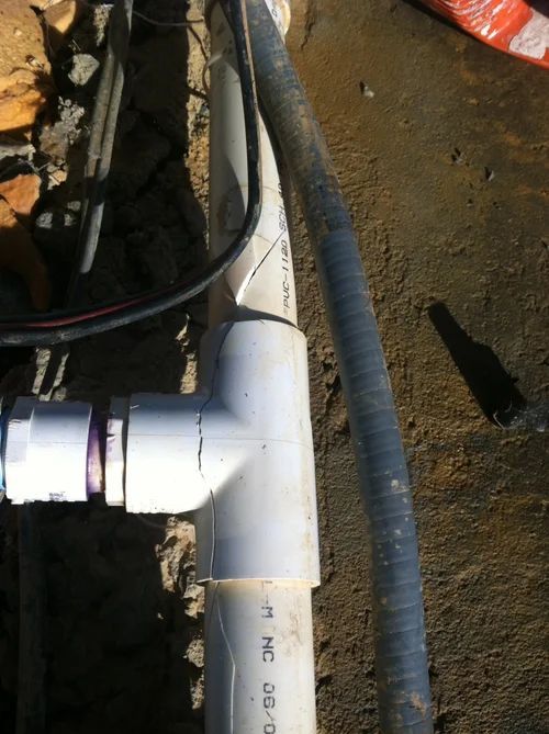 PVC pipe fittings and gray corrugated hose in a trench.