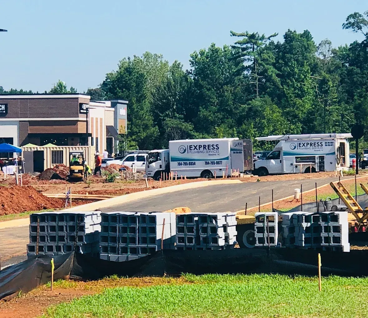 Construction site with cinder blocks in the foreground, Express Plumbing vans, and a building under construction.