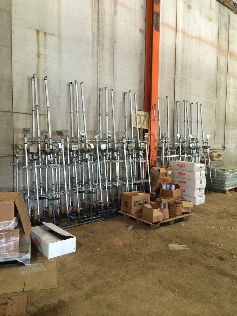 Metal plumbing pipes stacked against a concrete wall in a warehouse. Boxes and a pallet are in front.