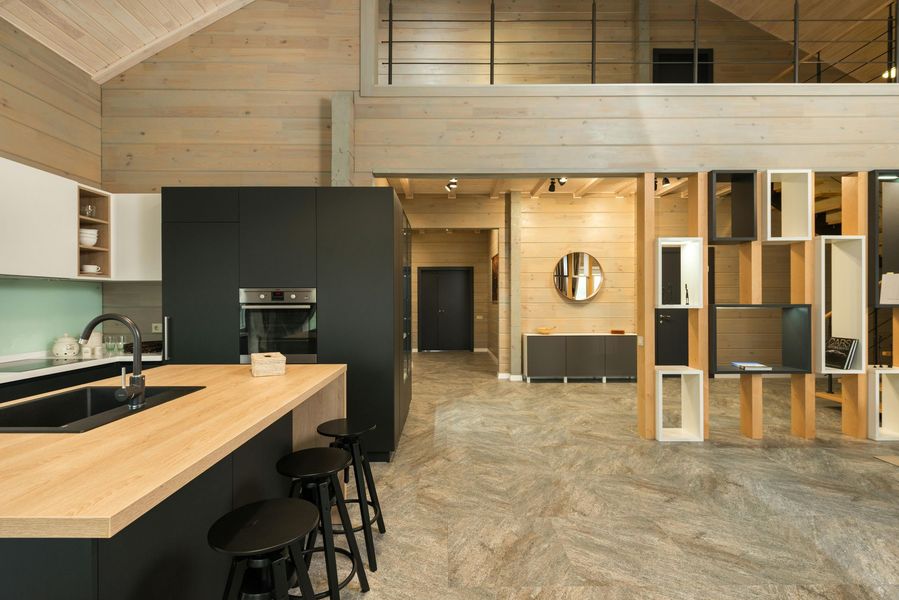 Modern kitchen with black island and wooden countertop, stools, and open shelving.