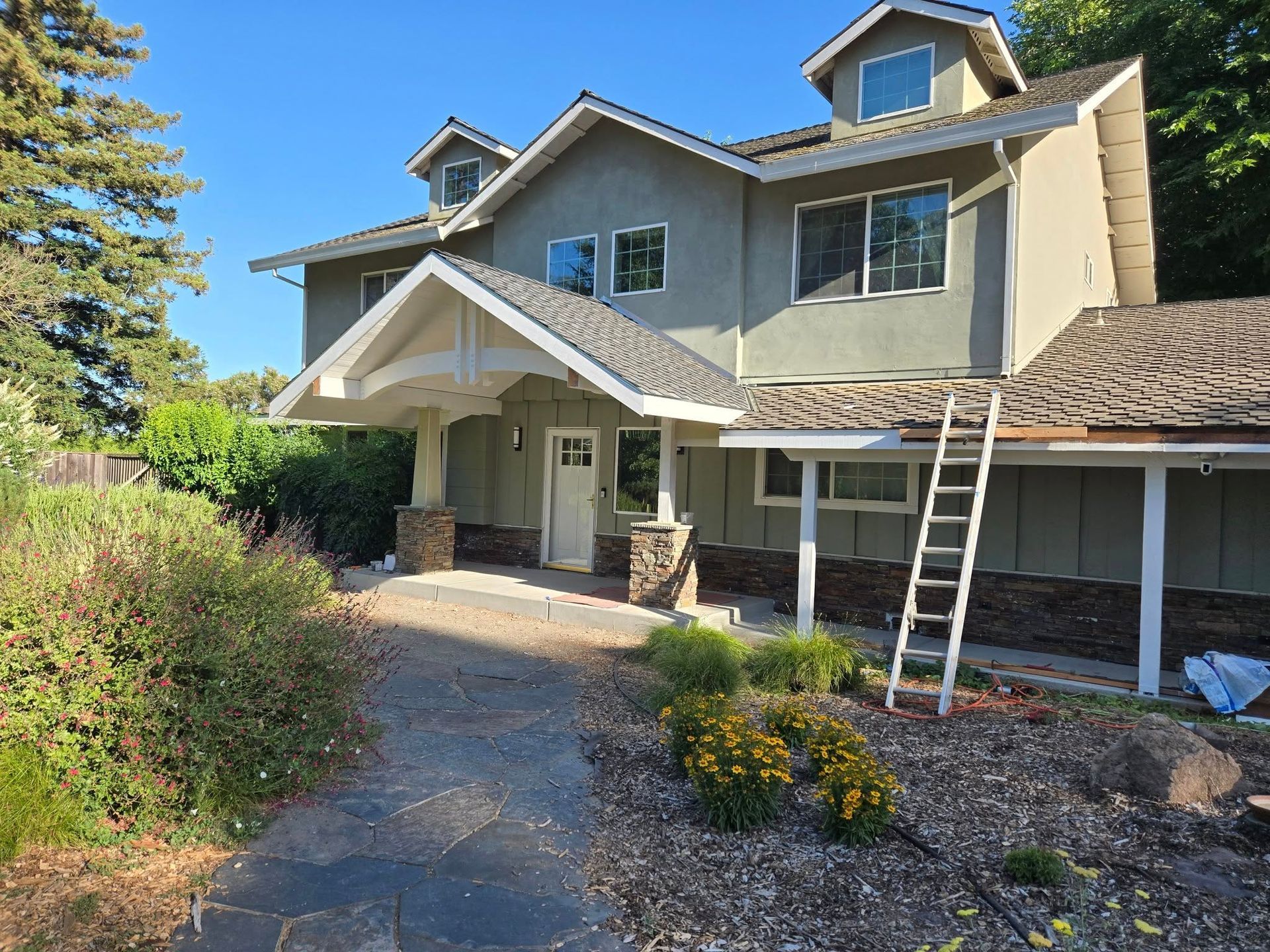 Two-story house with green siding, a brown roof, and a ladder leaning against the side.