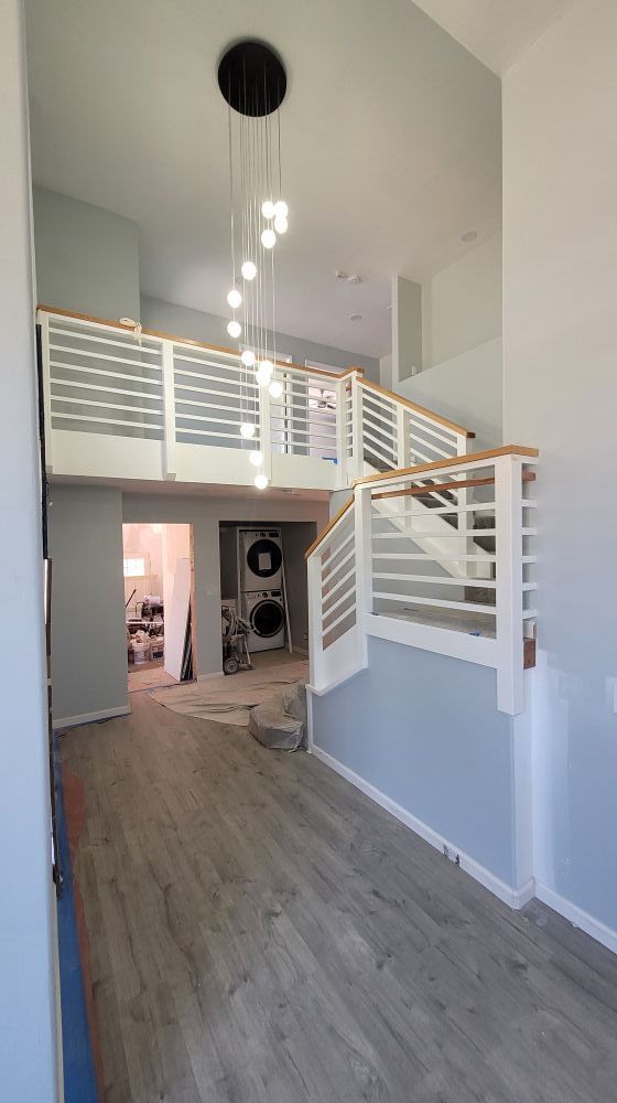 A two-story entryway with a staircase and a modern chandelier. White and wood railings. Light gray walls.