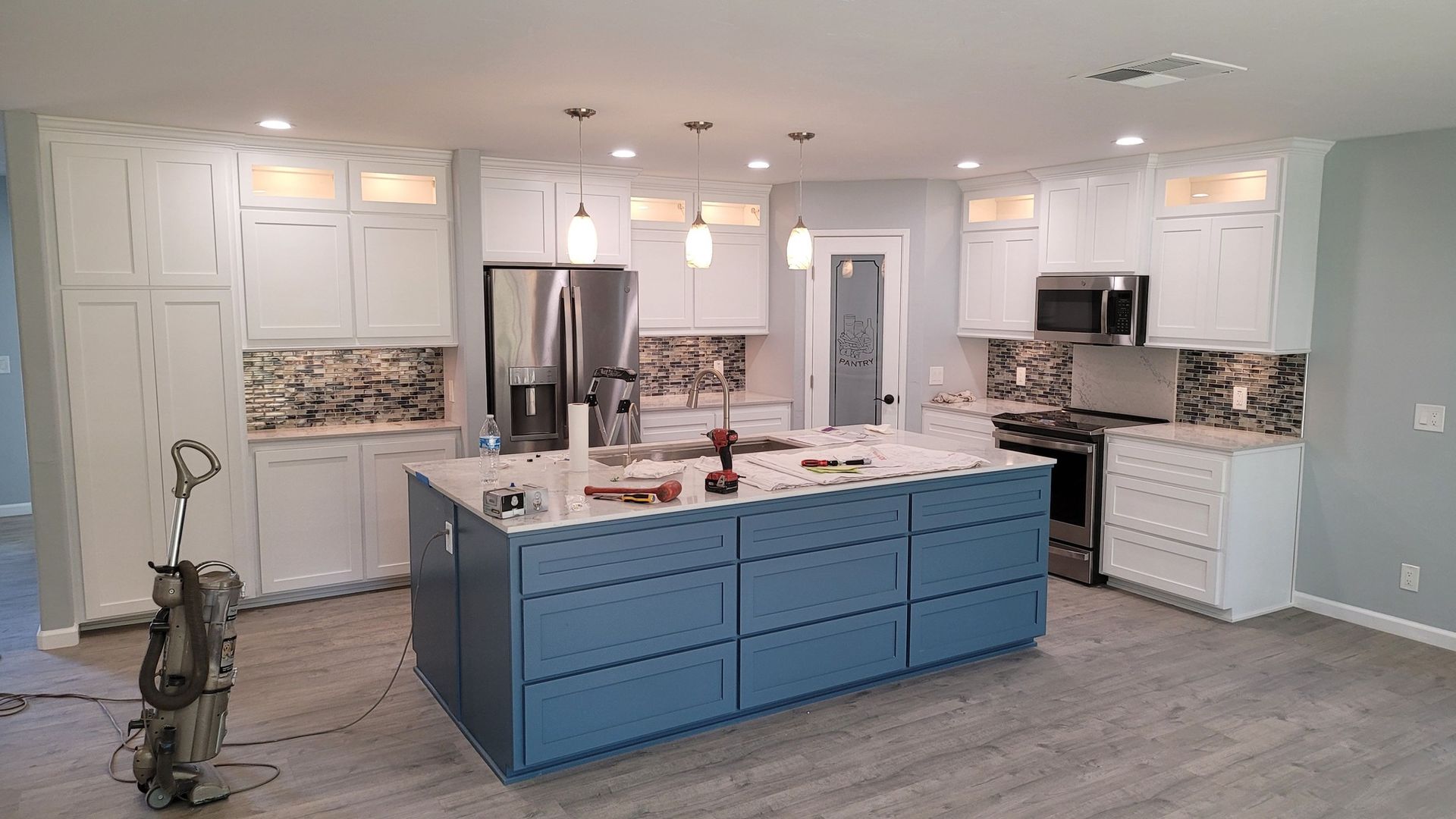 Modern kitchen with white cabinets, blue island, granite countertops, stainless steel appliances, and gray flooring.