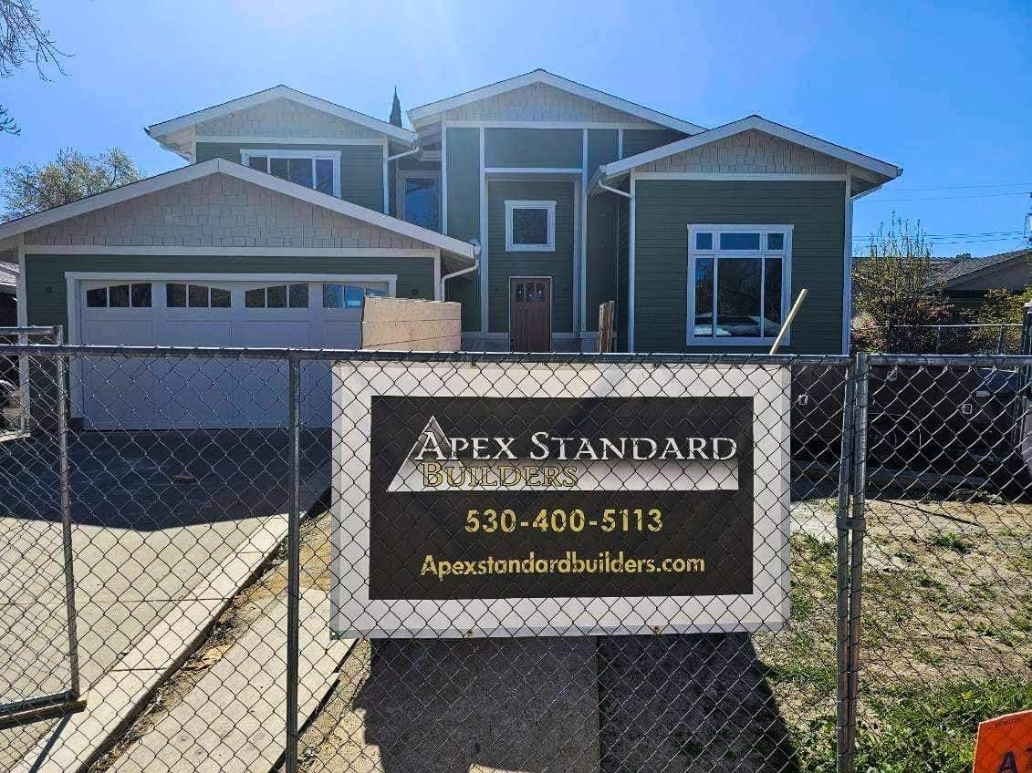 New green house behind a chain link fence with a sign for Apex Standard Builders.
