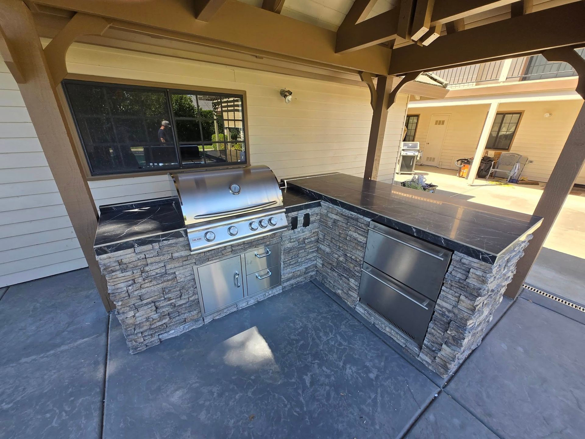 Outdoor kitchen with grill, countertops, and storage under a wooden pergola.