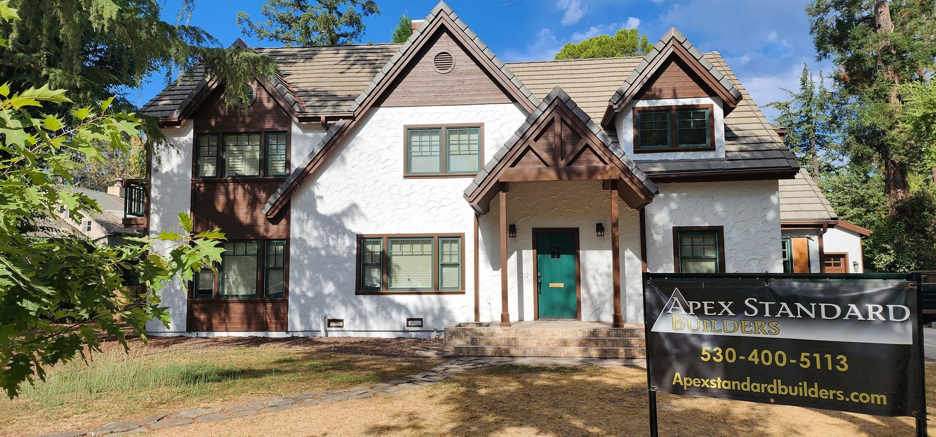 Tudor-style house with white stucco, brown trim, and a green front door; a sign says 