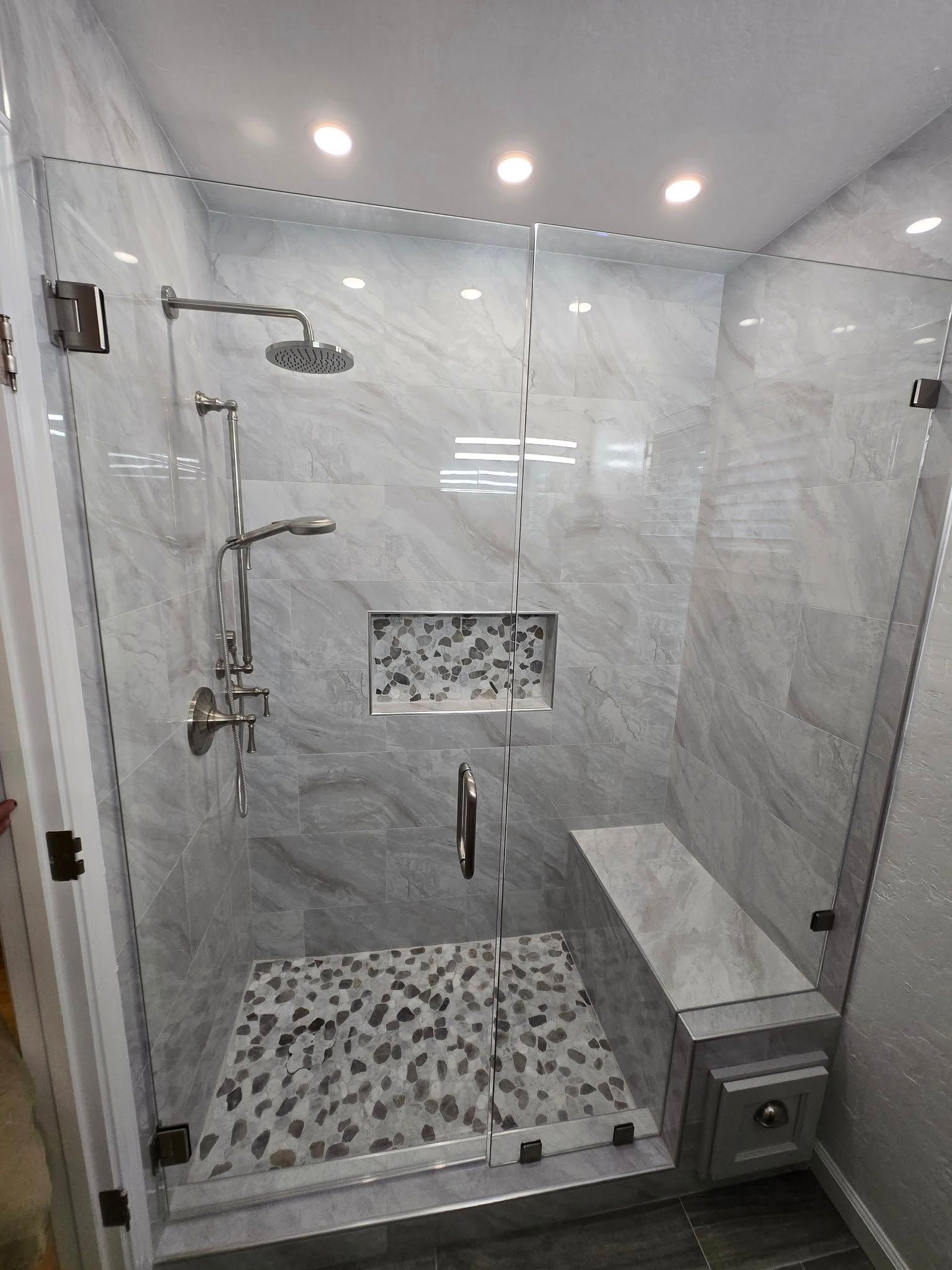 Modern shower with glass doors, gray marble tile, pebble floor, and built-in bench.