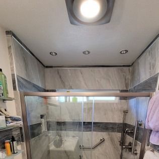 Bathroom with glass shower doors, marble tile, and overhead lighting.