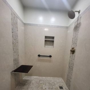 Bathroom with beige tile, showerhead, built-in shelf, grab bar, and foldable seat.